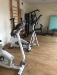 Wnętrze dziennego domu pomocy. Pomieszczenie rehabilitacji ruchowej. Po lewej stronie, pod ścianą, rowerek stacjonarny i steper. W głębi drabinka gimnastyczna zamocowana do ściany